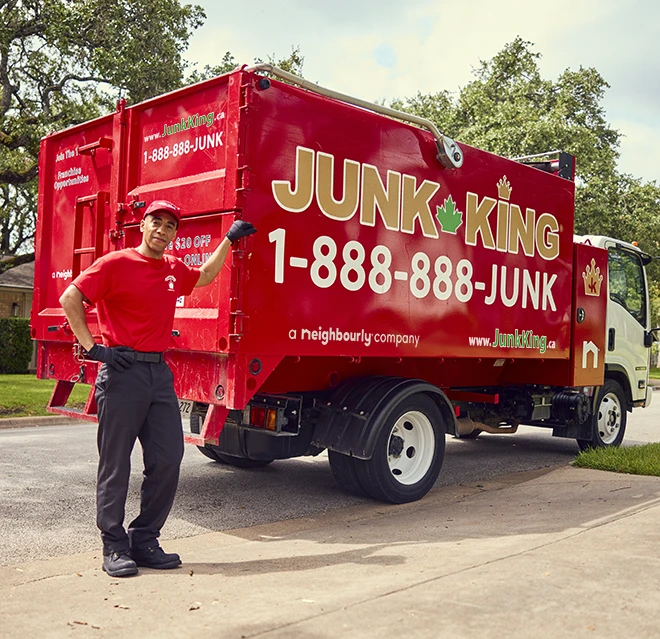 Junk King professional leaning against a red branded dump truck.